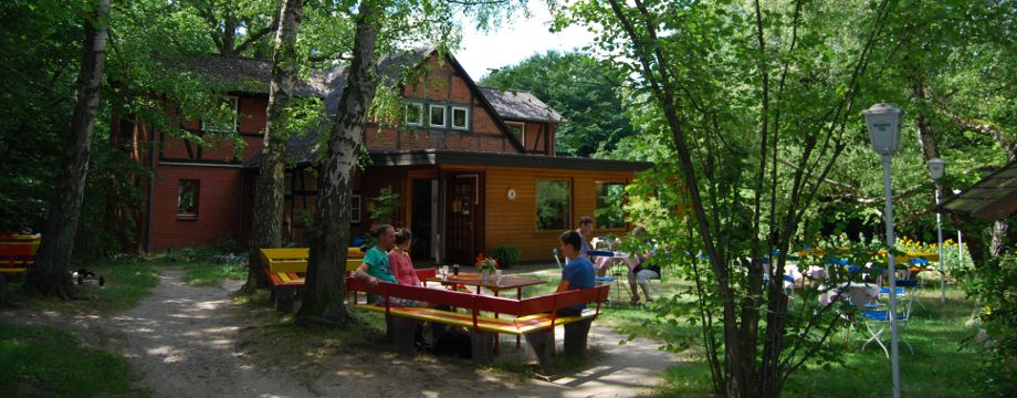 Urlaubsregion Höhbeck Elbe - Titelbild: Kaffeegarten Schwedenschanze inmitten des Ringwalls. Die Gäste sitzen auf rot-gelben Bänken unter Birken.